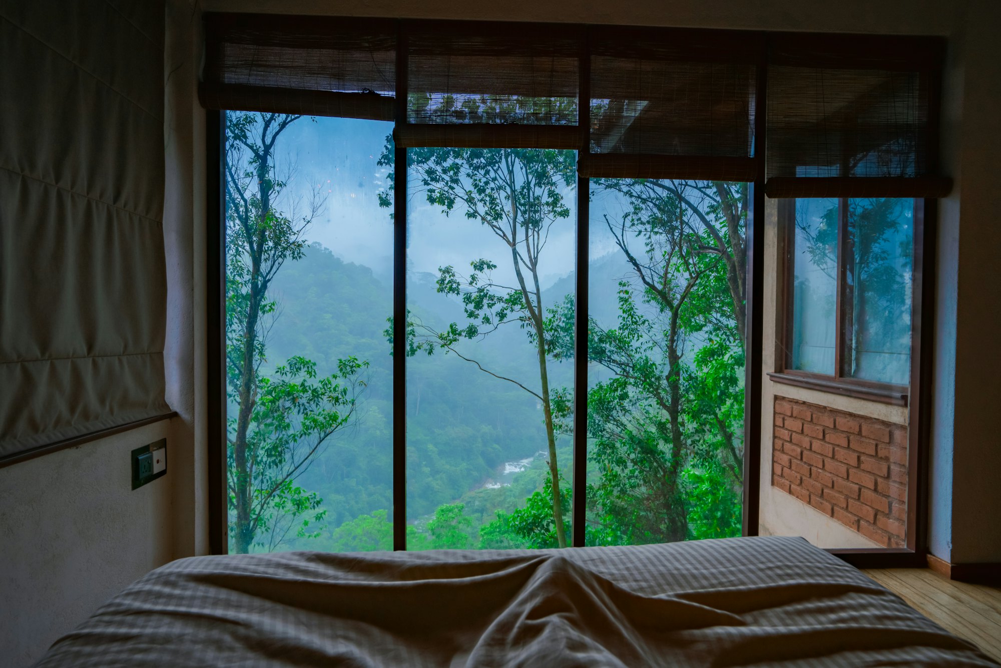 A second bedroom framed by timber windows onto the forested hillside
