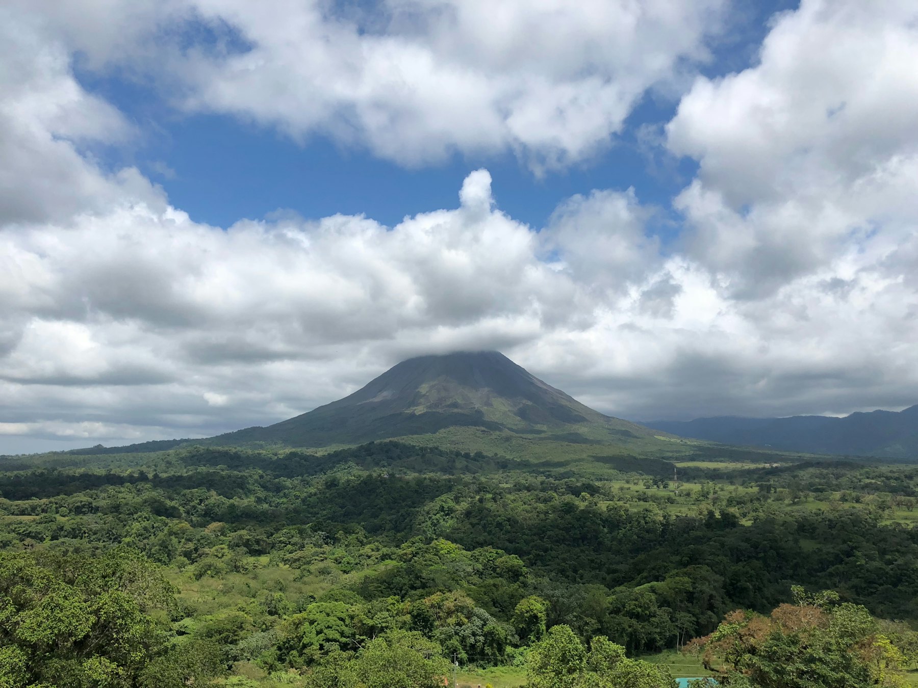 Volcano under cloud above forested lowland